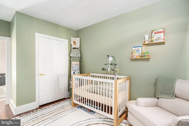 bedroom featuring a crib, wood finished floors, and baseboards