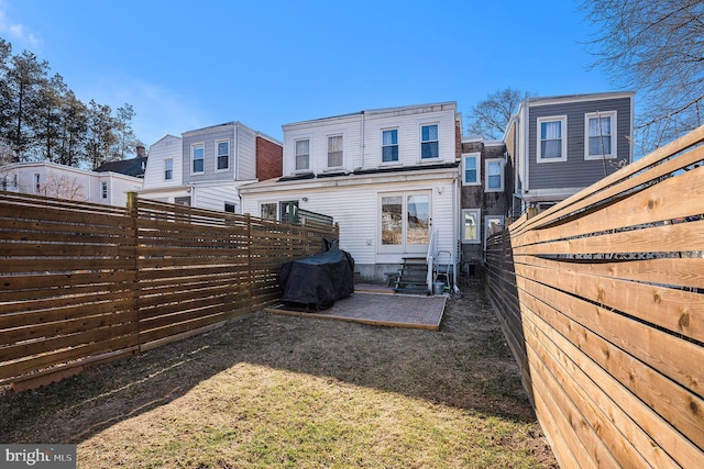 rear view of property featuring entry steps, a fenced backyard, and a lawn