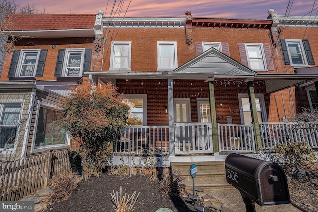 townhome / multi-family property with covered porch, brick siding, and fence