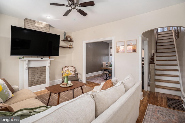 living area featuring arched walkways, wood finished floors, a ceiling fan, baseboards, and stairs