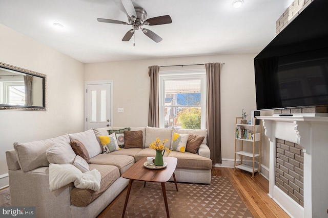 living area featuring light wood-style floors, a fireplace, baseboards, and a ceiling fan