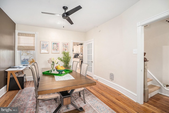 dining room featuring a ceiling fan, light wood-type flooring, baseboards, and stairs