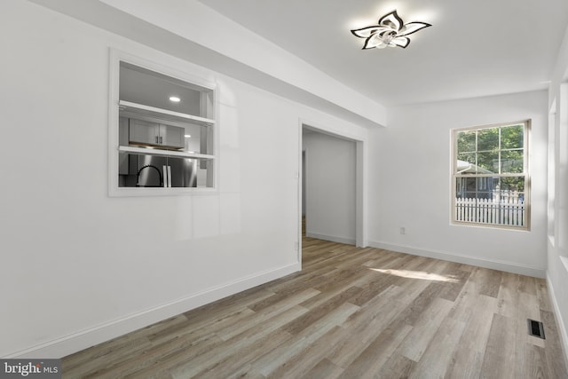 empty room with light wood-type flooring, visible vents, and baseboards