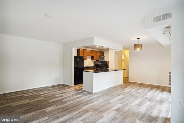 kitchen with pendant lighting, visible vents, stainless steel microwave, brown cabinetry, and freestanding refrigerator