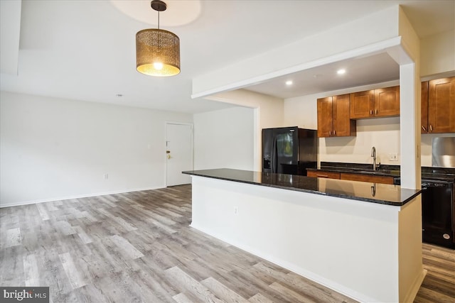 kitchen featuring light wood finished floors, a center island, black appliances, pendant lighting, and a sink