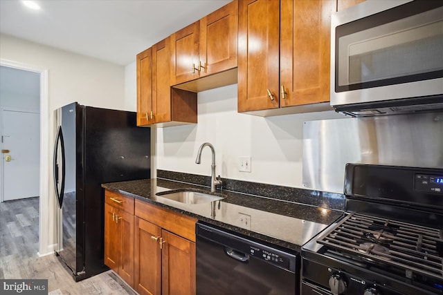 kitchen with light wood finished floors, dark stone counters, brown cabinets, black appliances, and a sink