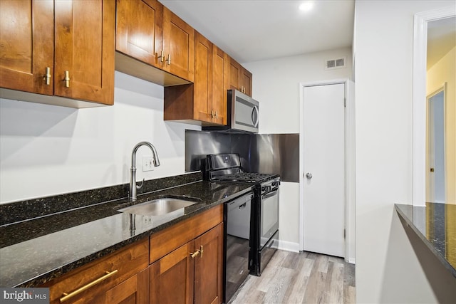 kitchen with a sink, visible vents, black appliances, brown cabinetry, and dark stone countertops