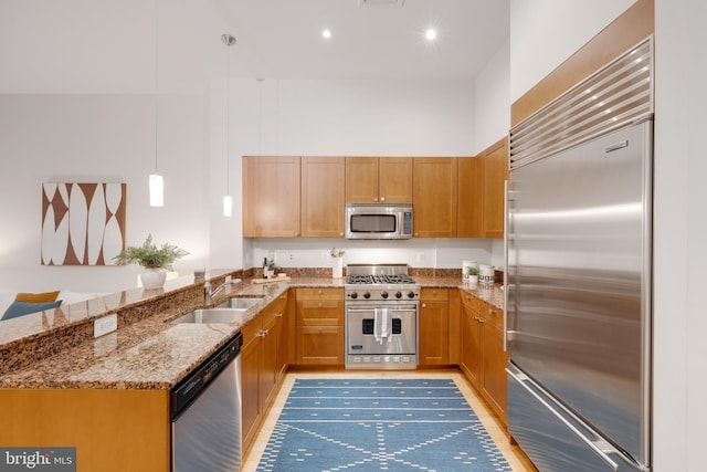 kitchen with decorative light fixtures, stone counters, a peninsula, high end appliances, and a sink