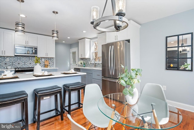 kitchen with stainless steel appliances, light countertops, light wood finished floors, and white cabinetry