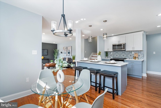 dining space featuring recessed lighting, baseboards, stairs, light wood finished floors, and an inviting chandelier