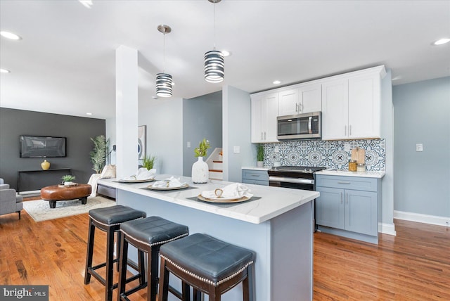 kitchen featuring light wood-style flooring, a kitchen bar, stainless steel appliances, and backsplash