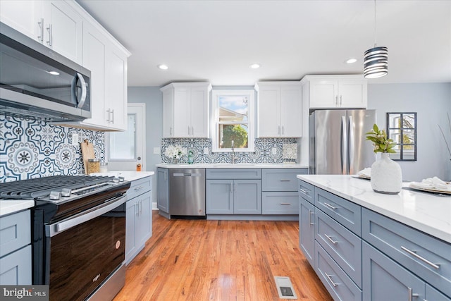 kitchen featuring light wood finished floors, white cabinets, stainless steel appliances, pendant lighting, and a sink