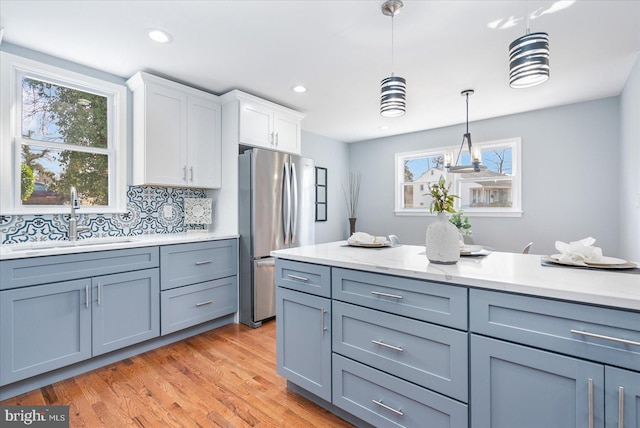 kitchen featuring light wood finished floors, white cabinets, decorative light fixtures, freestanding refrigerator, and a sink