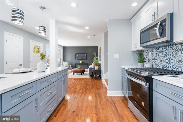 kitchen with white cabinets, decorative backsplash, stainless steel appliances, light wood-style floors, and pendant lighting