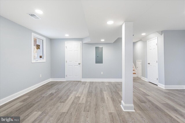 finished below grade area featuring light wood finished floors, electric panel, and baseboards