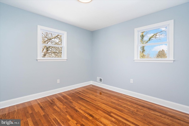 empty room featuring dark wood finished floors, visible vents, and baseboards