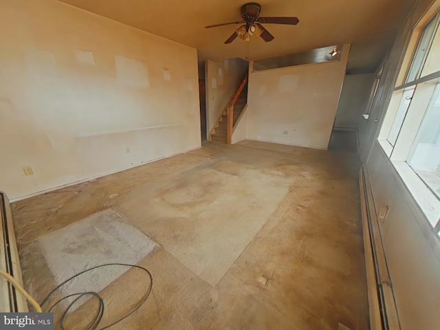 spare room featuring ceiling fan, stairway, and unfinished concrete floors