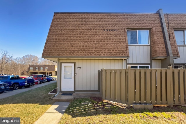 multi unit property with a shingled roof, fence, a front lawn, and mansard roof