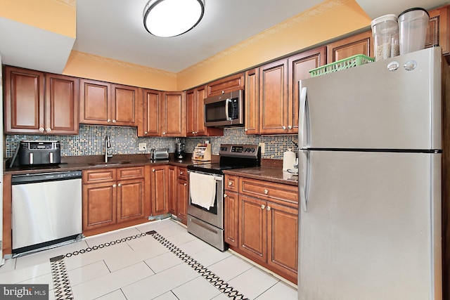 kitchen featuring decorative backsplash, dark countertops, appliances with stainless steel finishes, brown cabinets, and a sink