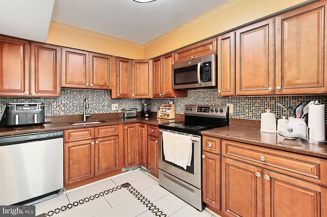 kitchen with brown cabinetry, appliances with stainless steel finishes, a sink, backsplash, and light tile patterned flooring