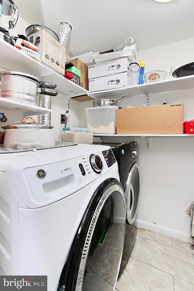 clothes washing area with laundry area, washer and clothes dryer, baseboards, and light tile patterned floors