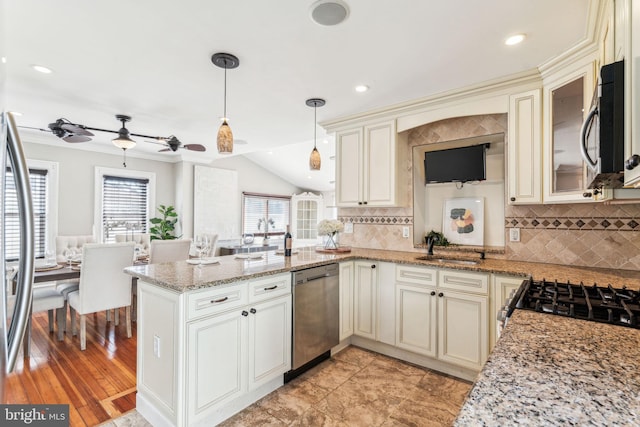 kitchen featuring stainless steel appliances, a peninsula, cream cabinetry, light stone countertops, and decorative light fixtures