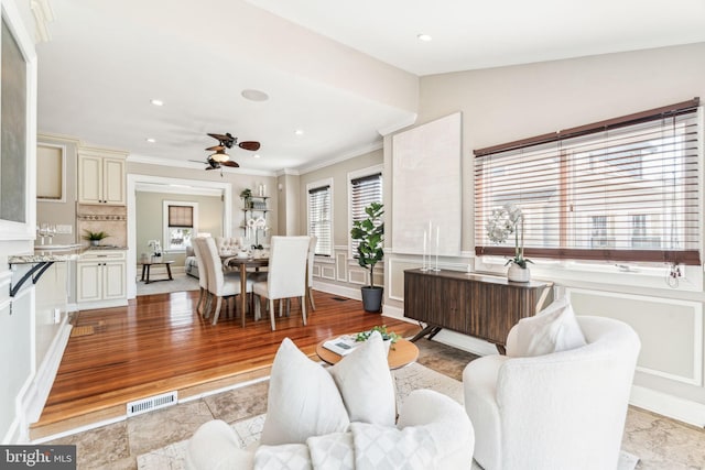 living room with a ceiling fan, visible vents, ornamental molding, and light wood finished floors