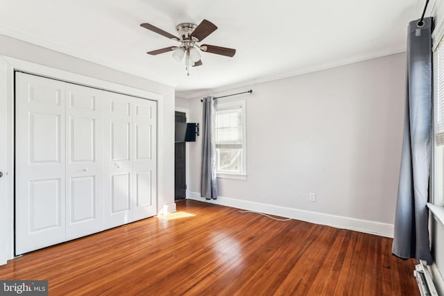 unfurnished bedroom with crown molding, a closet, ceiling fan, wood finished floors, and baseboards