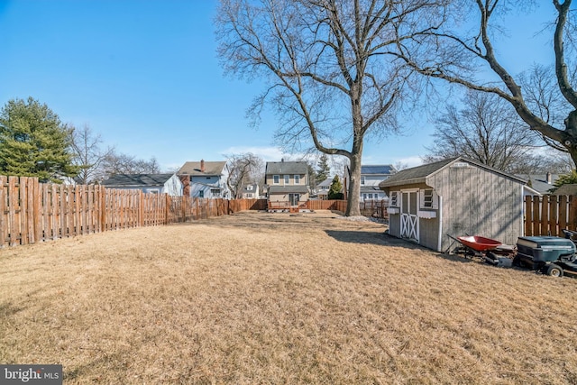 view of yard with a storage shed, a fenced backyard, a residential view, and an outbuilding