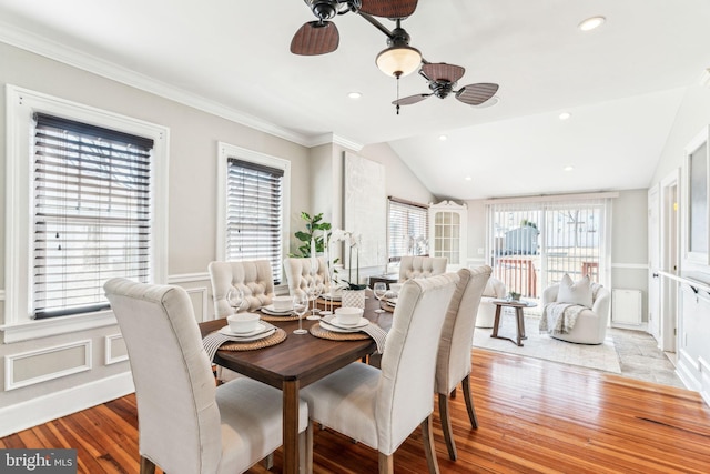 dining room featuring a wainscoted wall, a decorative wall, light wood-style floors, a ceiling fan, and vaulted ceiling