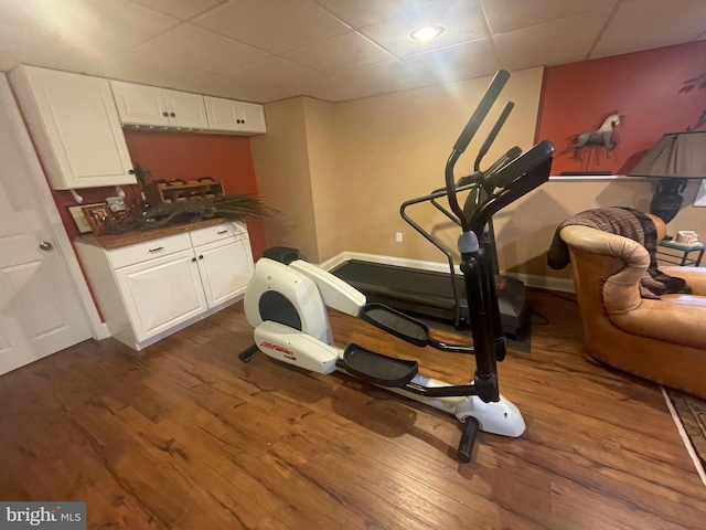 exercise area featuring dark wood-style flooring, a drop ceiling, and baseboards