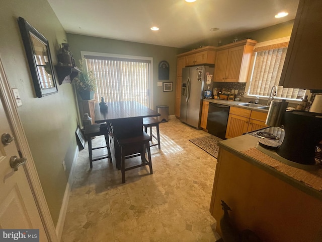 kitchen featuring stainless steel fridge, dishwasher, backsplash, light countertops, and a sink