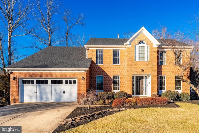 colonial inspired home with a garage, concrete driveway, roof with shingles, a front lawn, and brick siding