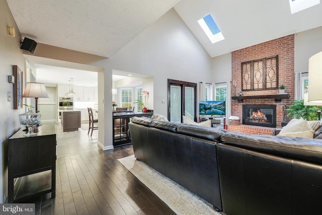 living area with a brick fireplace, a skylight, dark wood-style floors, and high vaulted ceiling