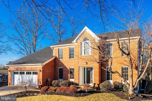 colonial inspired home with a garage, driveway, roof with shingles, and brick siding