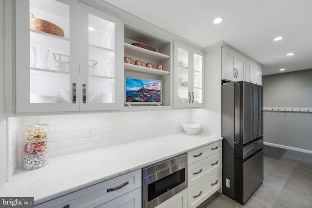 kitchen featuring white cabinets, freestanding refrigerator, tasteful backsplash, stainless steel microwave, and glass insert cabinets