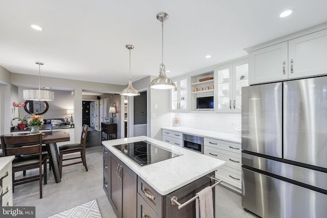 kitchen with light tile patterned floors, black electric stovetop, freestanding refrigerator, a center island, and tasteful backsplash