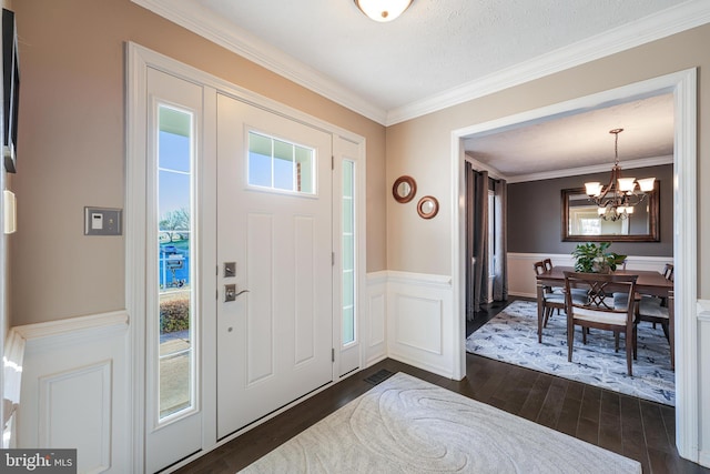 foyer entrance featuring wainscoting, dark wood-style floors, crown molding, a decorative wall, and a notable chandelier