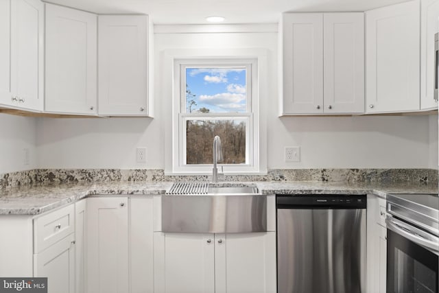 kitchen with light stone countertops, appliances with stainless steel finishes, white cabinets, and a sink