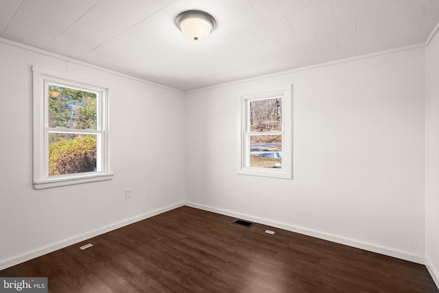 spare room featuring dark wood-style floors, visible vents, ornamental molding, and baseboards