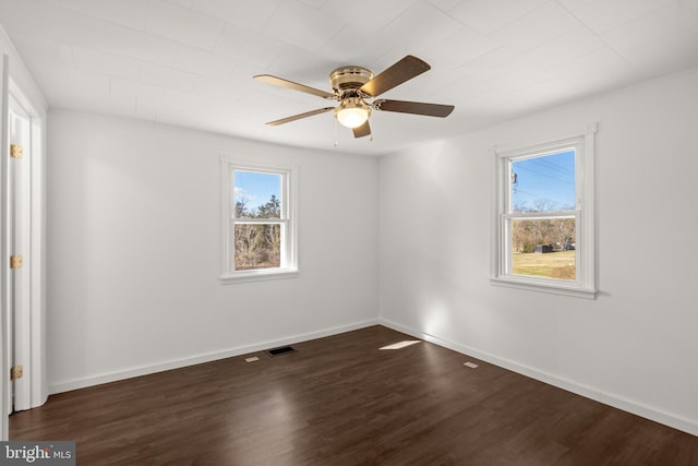 empty room featuring baseboards, dark wood-style flooring, visible vents, and a healthy amount of sunlight