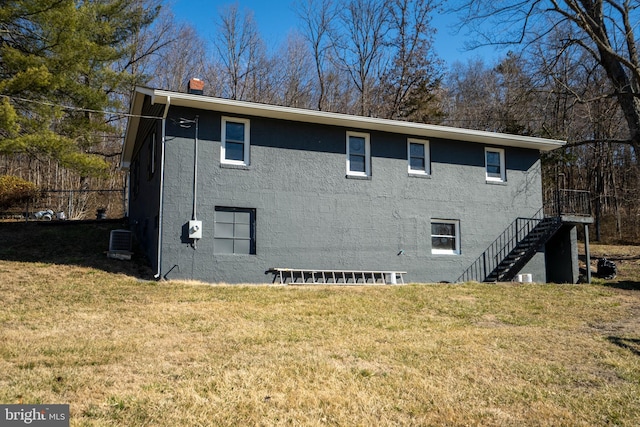 rear view of property featuring stucco siding, a chimney, stairway, and a yard