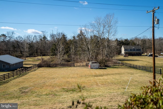 view of yard with a storage unit, a rural view, an outdoor structure, and fence