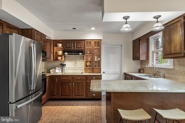 kitchen with under cabinet range hood, stainless steel appliances, a peninsula, a sink, and tasteful backsplash