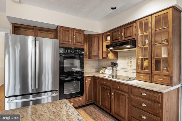 kitchen with backsplash, a textured ceiling, light stone countertops, under cabinet range hood, and black appliances