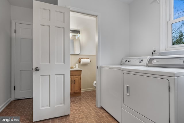 clothes washing area featuring brick floor, washer and dryer, laundry area, and baseboards