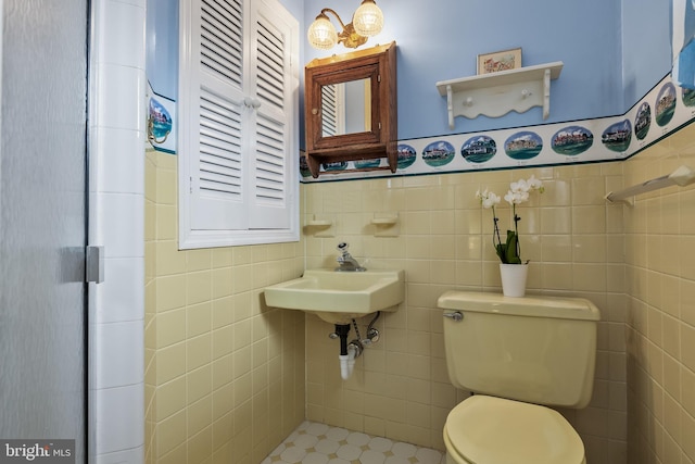 bathroom featuring wainscoting, a sink, tile walls, and toilet