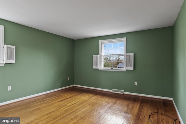 spare room with wood finished floors, visible vents, and baseboards