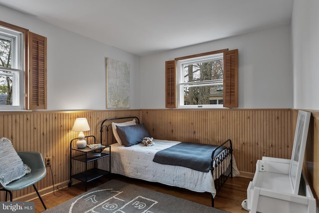 bedroom with wood finished floors, a wainscoted wall, wood walls, and multiple windows