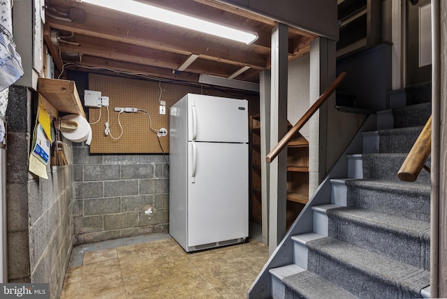 unfinished basement with concrete block wall, stairs, and freestanding refrigerator